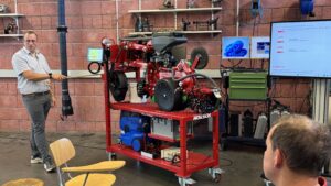 Schulung Sähmodell Horsch Ein Mann erklärt in der Werkstatt ein rotes Sähmodell auf einem Rollwagen, daneben sind Monitore und Werkzeuge zu sehen.